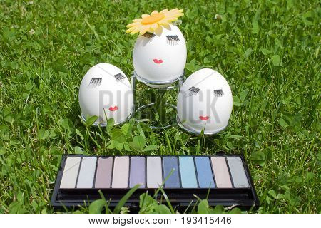 three eggs with make-up on a metal stand on green background in front of the kit eyeshadow