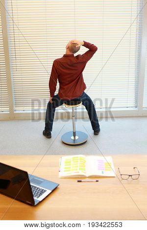 middle age man relaxing neck - short break for exercise on pneumatic stool in office