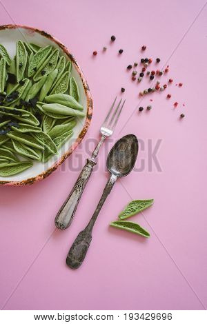 Dry green foglie pasta made from durum wheat semolina dried tomatoes spinach and water. Top view on vintage plate and old silver cutlery with champignons and pepper on pink background