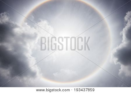 Sun with circular rainbow sun halo with gray clouds at noon.