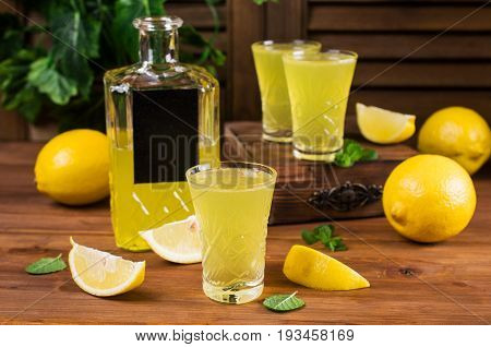 Italian traditional liqueur with lemons on a wooden background. Selective focus.