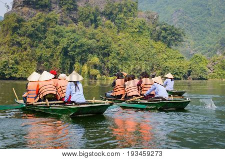 International tourists traveling on local vietnamese small boat along the Ngo Dong river of the Tam Coc Ninh Binh Vietnam.