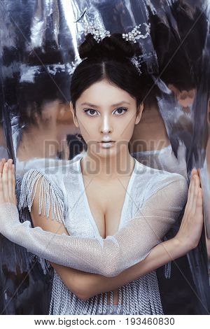 Portrait of futuristic young woman. Reflection of our mind and soul concept. Beautiful young multi-racial asian caucasian model cyber girl in silver urban clothes with conceptual hairstyle and make-up in metallik silver capsule.
