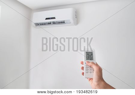 Hand holding remote control, adjusting temperature of air conditioner mounted on a white wall. Indooor comfort temperature