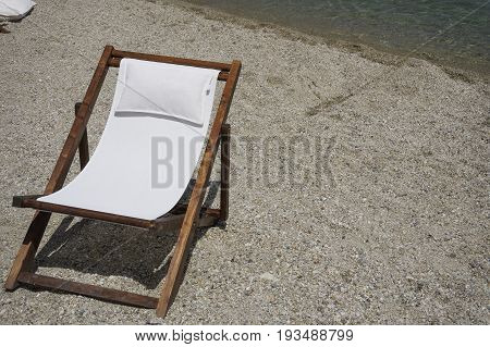 Wooden beach chair for tanning by the sea on a pebble beach.
Chaise longue deck beach chair with white texture seating on a summer sunny day.