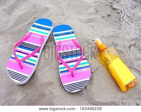 Summer time with flip-flops and sun-care milk on a sandy beach