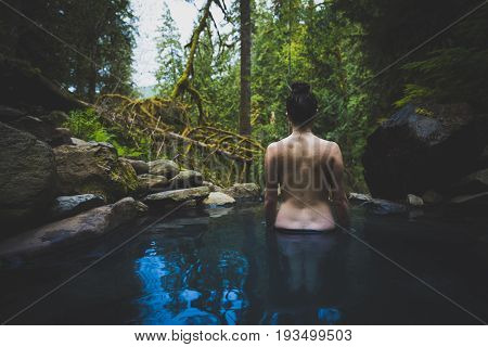 Young caucasian woman standing in natural hot spring bare back.