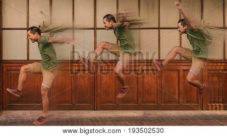 Image with multiple exposure of a casually dressed young Asian man, with a backpack jumping outside in front of windows in the city with motion blur