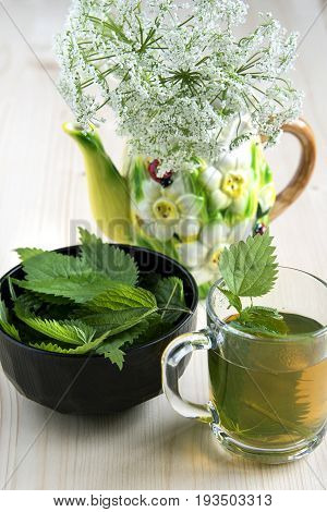 Nettle tea on the wood background leaves in the cup on a wooden table and wild flowers