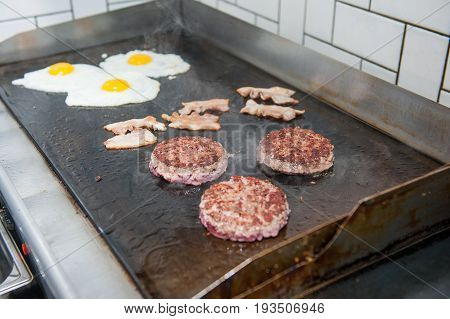 Burger Restaurant Menu Cooking Process. Eggs, Cutlets And Bacon Are Fried On A Grill. Fast Food Cafe