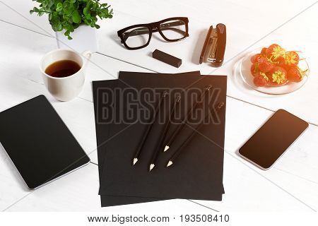 Modern workplace with digital tablet computer and mobile phone, cup of coffee, pen and empty sheet of paper. Top view and copy space for text. sun flare