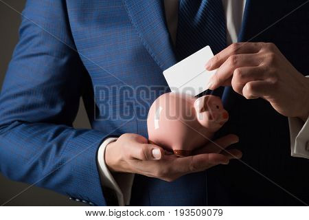 Hands Putting Blank Business Card In Piggy Bank