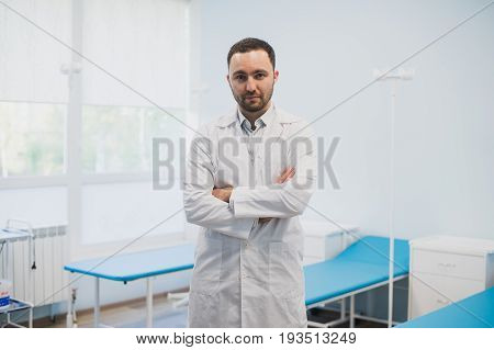 Portrait of a serious confident male doctor standing with arms crossed at medical office.