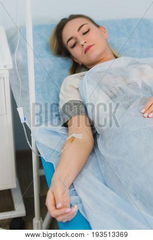 Pensive woman transfused lying in hospital ward.