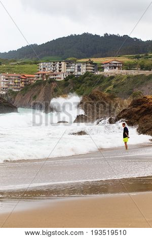 BAKIO SPAIN - JULY 4 2016: Unknown tourists on a beach. The young man costs on the beach and observes a storm