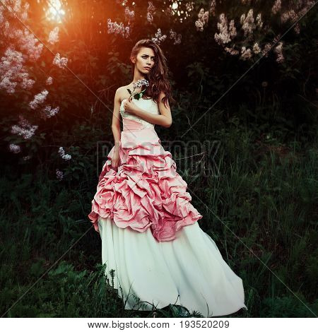 Beautiful and elegant woman with branch of lilacs and hair waves wearing wine red and white dress posing outdoors retro vintage style and fashion. She looks like a runaway bride with dramatic emotion