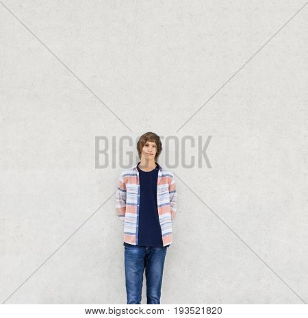 Young Boy With Trendy Haircut Wearing Shirt And Jeans Standing Near White Concrete Wall Having Serio