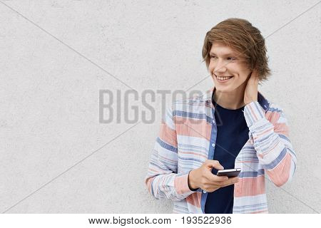 Portrait Of Fashionable Guy With Stylish Hairstyle Wearing Shirt Holding Smartphone Messaging Online