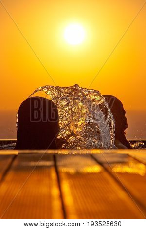 Silhouettes of swimming girls and splashing water against the sea and the setting sun in Pomos village in Cyprus