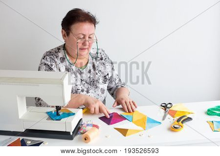 needlework and quilting in the workshop of a tailor woman - elderly women tailor put on the desktop pieces of colored fabric, lay next to the scissors, buttons, pins and thread for sewing machine