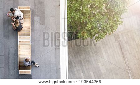 top aerial view of people sit on wood bench at the upper floor pedestrian with the lower floor of tree garden and street.