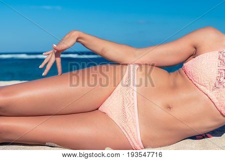 Tanned sexy legs of a woman against the sea, tropical beach scene.
