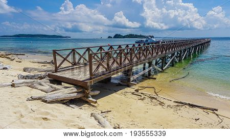 Wooden jetty over the beautiful Rusukan Besar island tropical beach with blue sky and clouds in Labuan Pearl of Borneo,Malaysia.