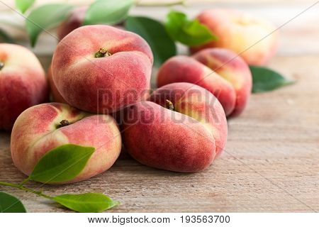 Fresh peaches with leaves on wooden background. Doughnut or vineyard type of flat peach.