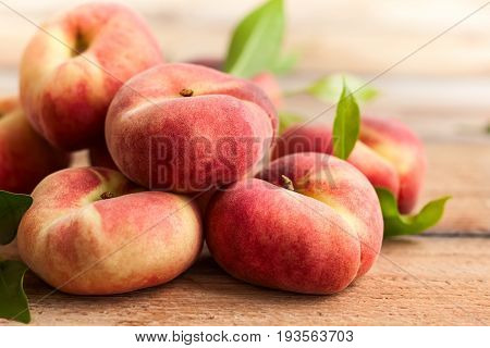 Fresh peaches with leaves on wooden background. Doughnut or vineyard type of flat peach.