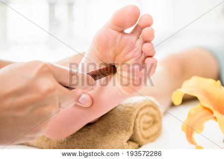 Professional therapist giving traditional thai foot massage with stick to a woman in spa