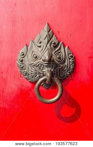 The ancient thai styles door handle or door knocker made from brass on red door.