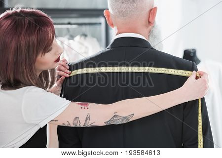 young tailor fitting grey haired man with measuring tape