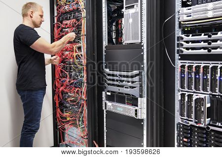 Side view of mid adult male IT consultant checking with network cables connected to servers in datacenter