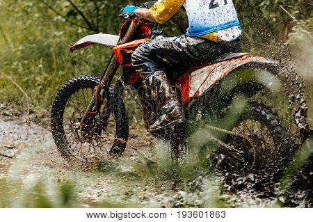 motocross enduro athlete on motorcycle crosses a puddle of water and mud