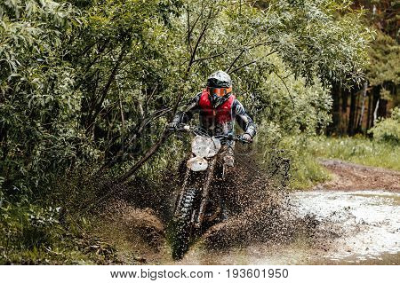 enduro athlete on motorcycle crosses a puddle of water and mud racing motocross