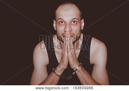 Prayer. Arrested criminal man with handcuffs on his hands pray to God. Isolated on black background.