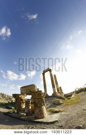 wide shot showing anceint columns standing and blue sky background with sun flair in amman citadel