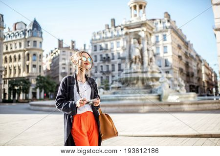 Young woman standing with photo camera on the Jacobins square with famous fountain on the background in Lyon city in France