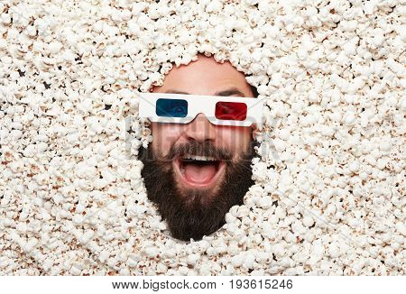 From above shot of bearded man wearing stereo glasses lying in popcorn and looking excitedly at camera.