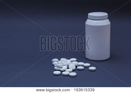 White pills medicine and plastic bottle behind on dark gradient background