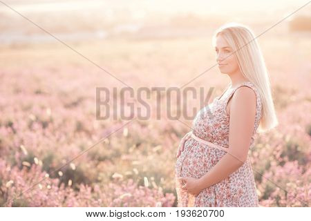 Smiling pregnant woman 25-29 year old resting in lavender field. Posing outdoors. Motherhood. Maternity. 20s.