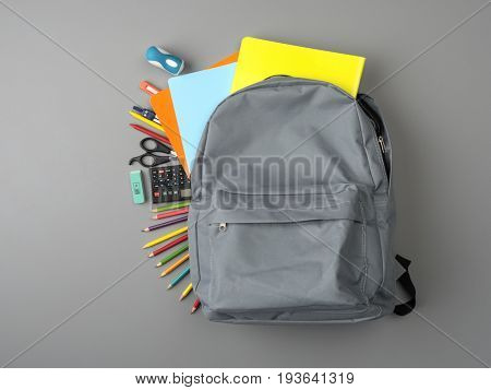Top view of a backpack and school supplies on grey wooden table