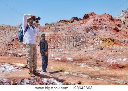 Hormuz Island Hormozgan Province Iran - 17 april 2017: Iranian Island of Hormuz in Persian Gulf the guide is watching a tourist who takes photos of salt glaciers in salt mountains.