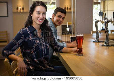 Portrait of young friends with drinks at counter in bar