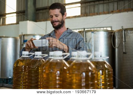 Smiling working taking a photo of olive oil bottles in factory