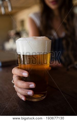 Close-up of barmaid holding beer glass at counter in bar