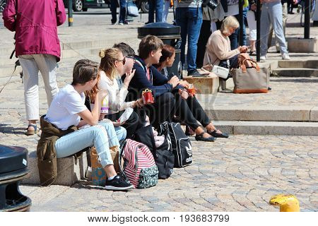 Stockholm, Sweden - June 27 2017: Unknown people snack fast food from fast cafes. Tourists sit on the quay on the pavement sidewalk in the center of the city. Concept of healthy eating.
