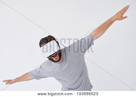 Close-up shot of energetic beardman in VR glasses stretching his hands out as if flying, isolated on white background 