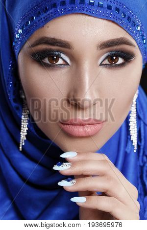 Gorgeous Young East Woman face portrait in hijab. Beauty Model Girl with bright eyebrows, perfect make-up, touching her face. Traditional. Isolated on black background. Smokey.Jewelry on her face.Studio