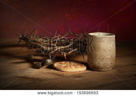 Crown of thorns, cup of wine, bread and nails over wooden table